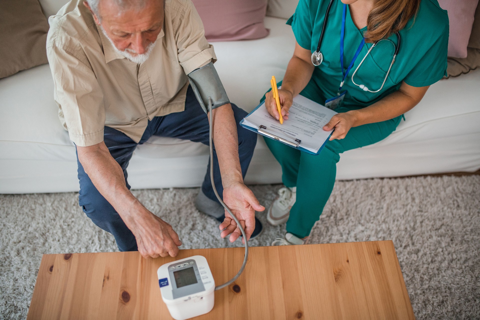 An unrecognizable female nurse keeps records during a home visit to a senior man and blood pressure measurement